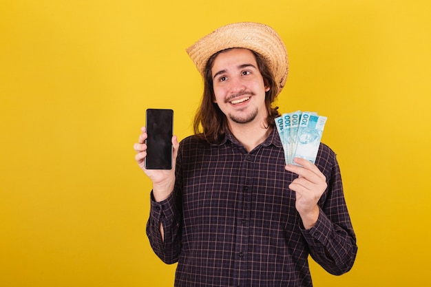 Man met typische kleding voor feest junina holding geld en mobiele telefoon geld apps