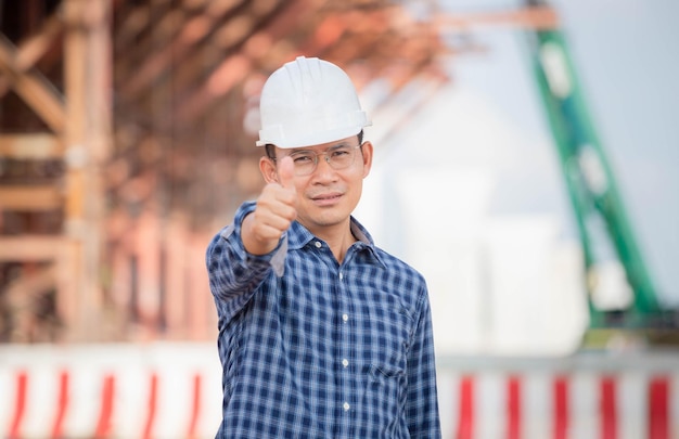 Man met veiligheidshelm duimen opdagen op de bouwplaats van de infrastructuur Ingenieur controleert project op de bouwplaats