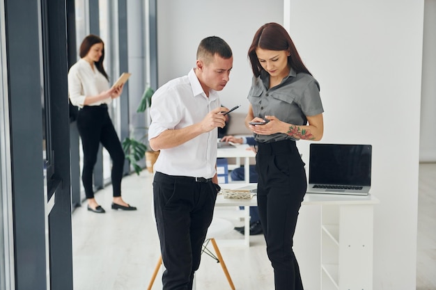 Man met vrouw die telefoon gebruikt Groep mensen in officiële formele kleding die binnenshuis op kantoor is