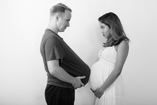 Man met watermeloen als maag en zwangere Aziatische vrouw samen als multi-etnisch getrouwd stel in zwart-wit