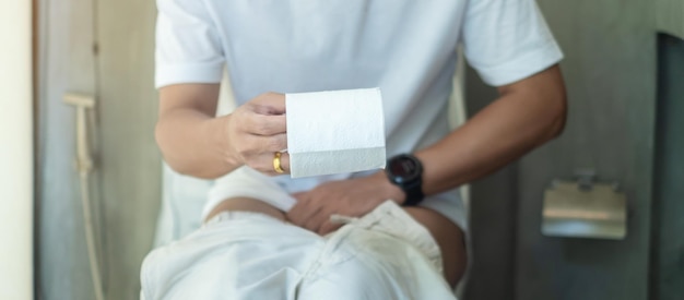 Man met wc-papierrol tijdens het zitten op de wc-pot diarree verstopte menstruatieinfectie abdominale buikpijn cystitis Verzekering en medisch concept