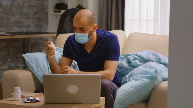 Man met wegwerpmasker wijzend op pillen in een videoconferentie met zijn arts tijdens quarantaine van het coronavirus.