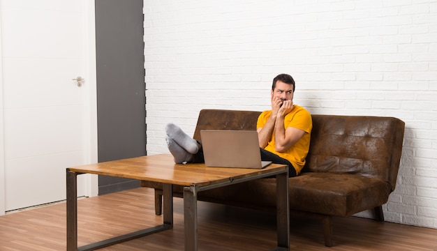 Man met zijn laptop in een kamer is een beetje nerveus en bang om zijn handen op de mond te leggen