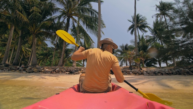 Man met zonnebril rijd roze plastic kano langs zee tegen groene heuvelachtige eilanden met wilde jungles