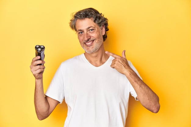 Man in the midst of a shaving routine with an electric razor on a yellow backdrop