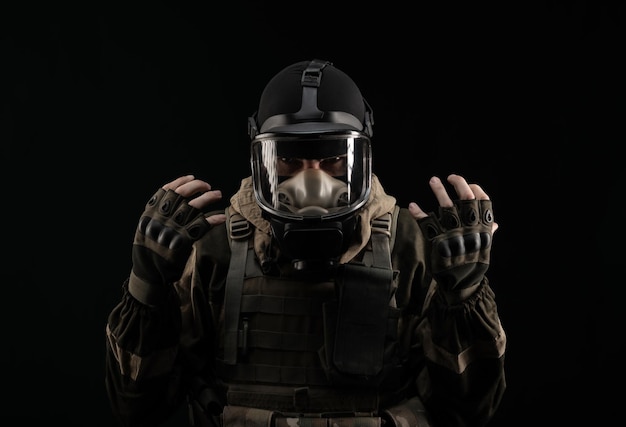 A man in a military uniform and a gas mask holds with an angry expression of emotions on a black background