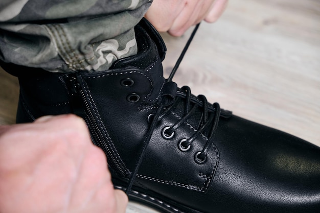 Man in a military uniform ties the laces on his black shoes.