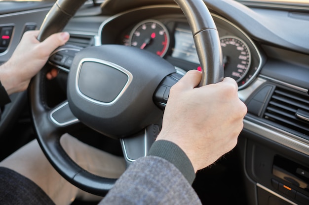 Un uomo in un'auto moderna. mani che tengono il volante nella posizione corretta.