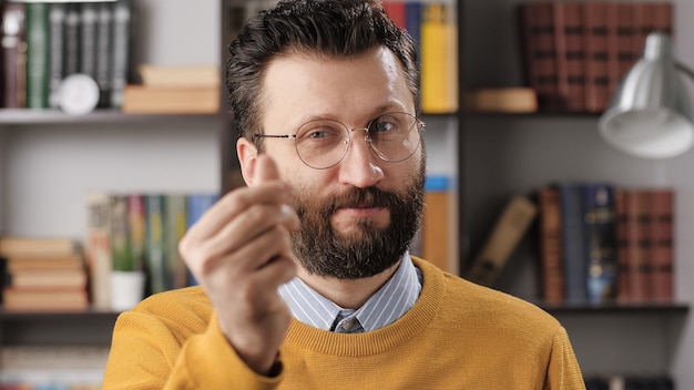 Emozione di gesto di denaro uomo. insegnante maschio barbuto o uomo d'affari con gli occhiali che guarda l'obbiettivo e mostra il gesto della mano dammi soldi. colpo medio