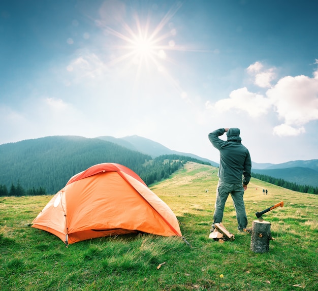 Man on mountain near orange tent looks into the distance