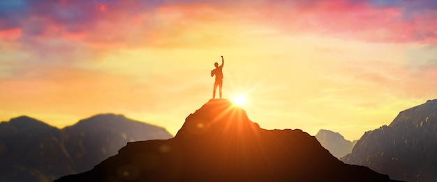 Man on mountain peak with open arms welcoming new day with\
sunrise success successful man with hands up on peak of mountain at\
sunset successful person