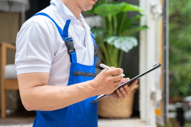 Man mover in uniforme blu controlla le liste sugli appunti mentre scarica le scatole di cartone dal camion