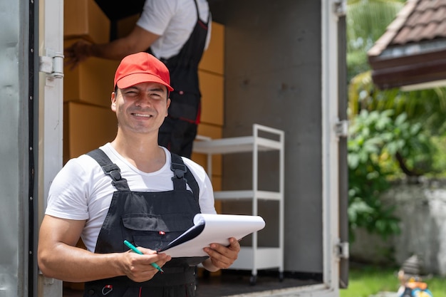 Photo man mover worker checking lists on clipboard while unloading cardboard boxes from truck