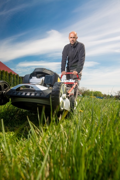 男が刈る、彼の巨大な庭の庭で草を刈る、モーターガーデン芝刈り機による緑の野原、ガーデニングの概念