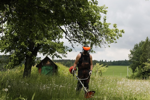 Man mowing tall grass with petrol lawn trimmer in the garden or backyard Process of lawn trimming with hand mower