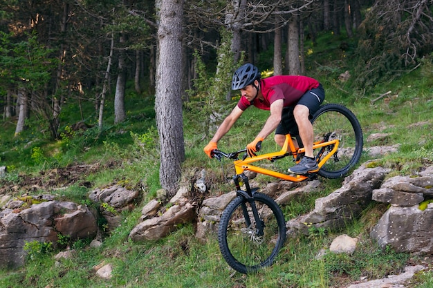 Man naar beneden rotsen in een bos op de mountainbike