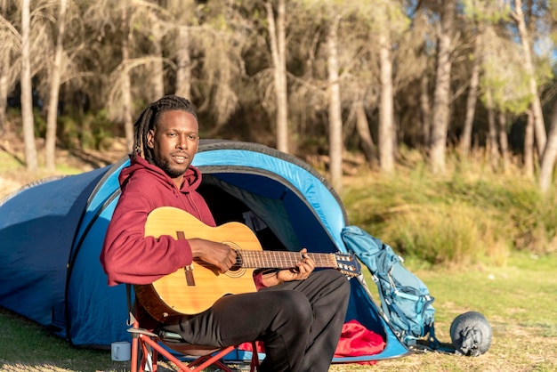 A man near the camping tent with a guitar enjoying nature