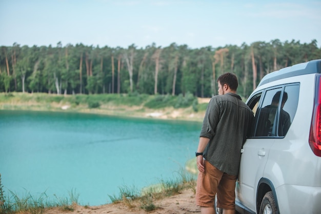 青い水で湖を見ている端に白いsuv車の近くの男