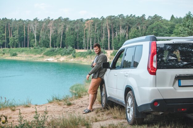 Man near white suv car at the edge looking at lake with blue water