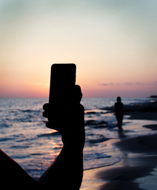 Foto man neemt een zonsondergangfoto van vriendin op de mobiele telefoon