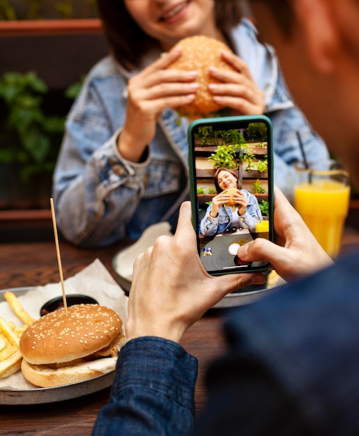 Foto man nemen foto van vrouw hamburger eten