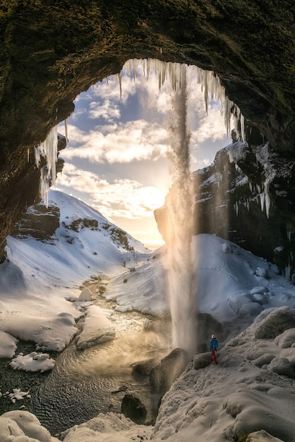 Man observing waterfall in snowy cave at sunset