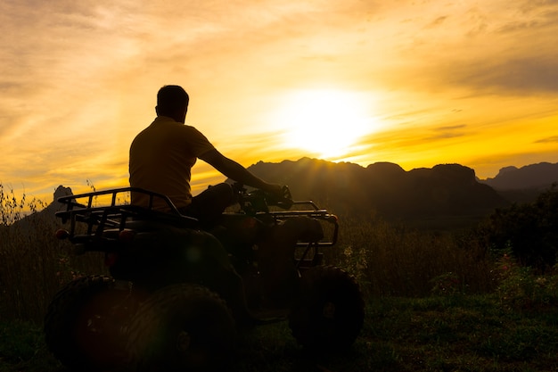 写真 大きな山の上の日没を見ているatv車の男。シルエットの肖像画。