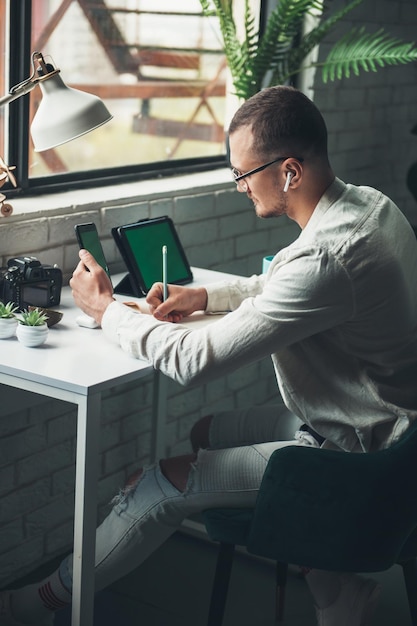 Man ondernemer in brillen zitten en werken aan tafel schrijven in planner met smartphone en