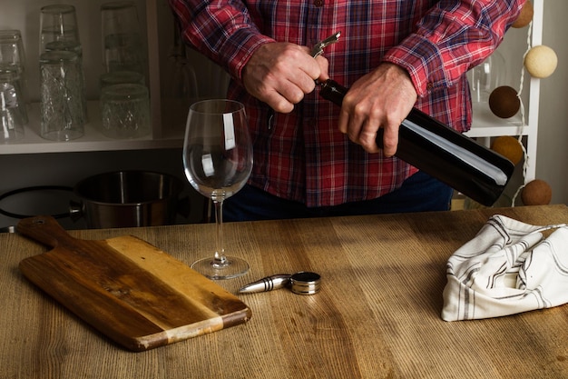 Foto man ontkurkt een fles rode wijn op een houten tafel