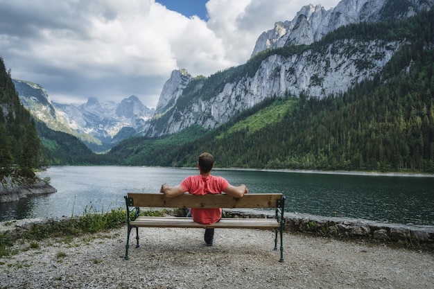 Man ontspannen op bankje voor Dachstein-gebergte weerspiegeld in Gosau meer Oostenrijk