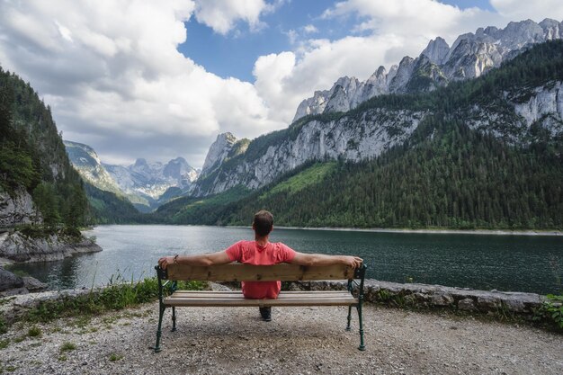 Man ontspannen op bankje voor Dachstein-gebergte weerspiegeld in Gosau meer Oostenrijk