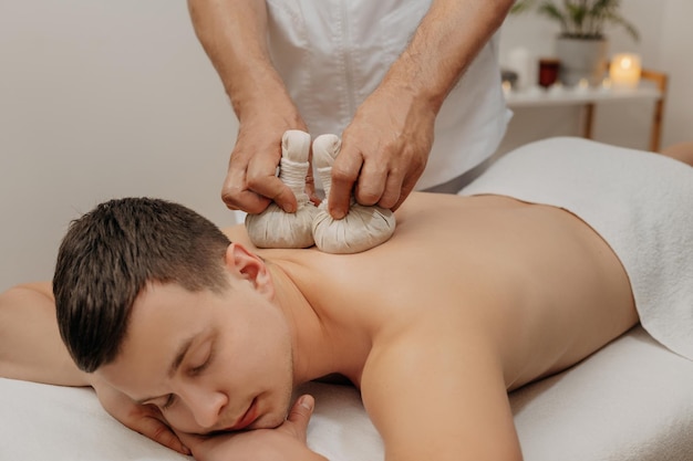 Man ontspannen tijdens traditionele Thaise kruidenmassage. Oosterse geneeskunde met aromazakjes.