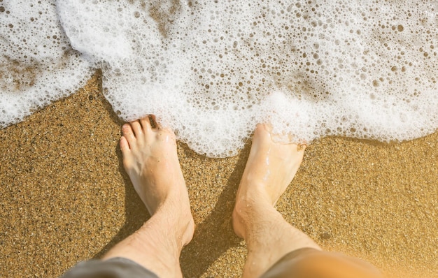 Man ontspant blootsvoets op het strand Guy's benen op het zand Golven aan de oceaanzijde Zomervakantie Reisconcept