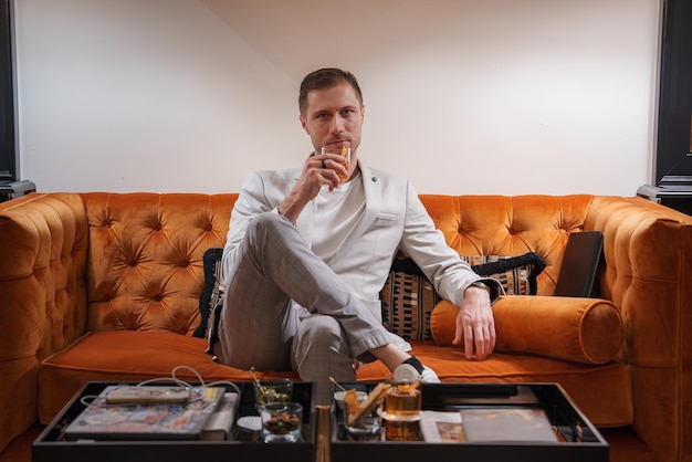 Foto man ontspant zich op een oranje leren bank met een glas whisky in een moderne woonkamer