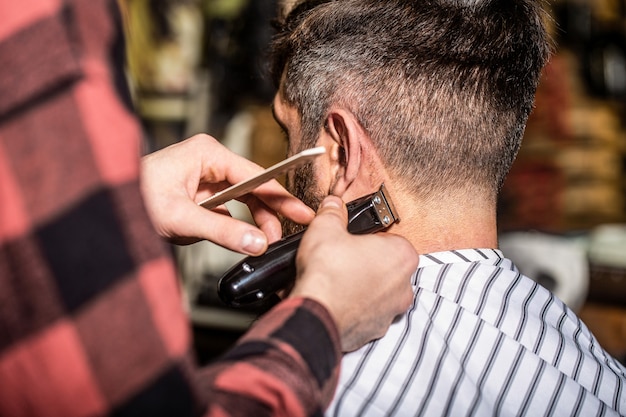 Man op bezoek bij kapper in herenkapper. Kapper werkt met tondeuse