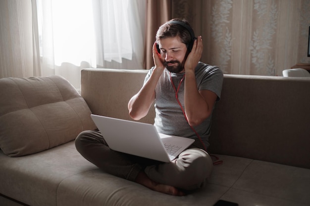 Man op de bank met koptelefoon en notebook thuis