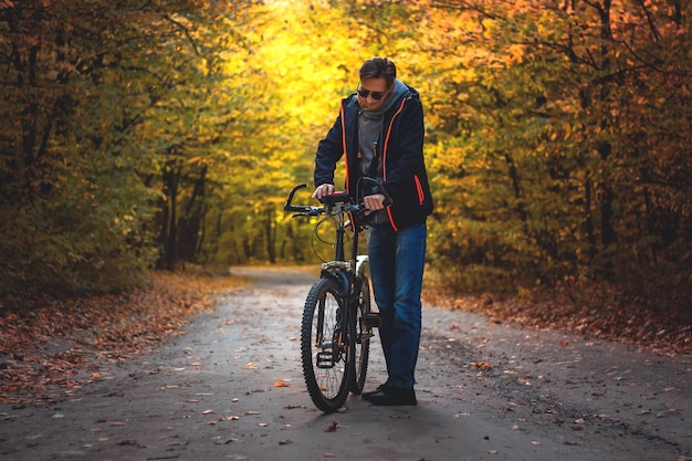 Man op een fiets in het herfstbos in de avond bij zonsondergang