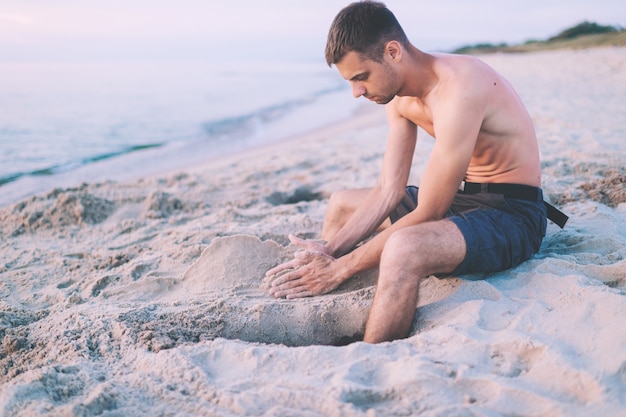 Man op het strand zandkasteel bouwen