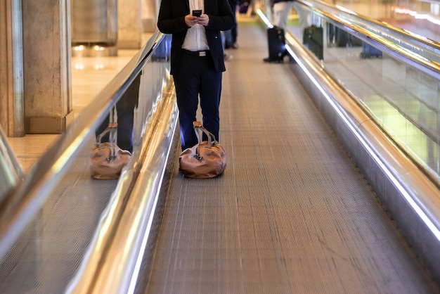 Man op roltrap op de luchthaven met behulp van mobiele telefoon met bagage