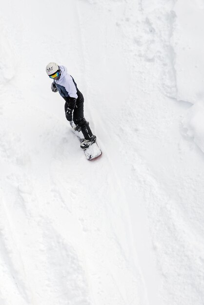 Man op snowboard in uitrusting daalt af van besneeuwde berghelling