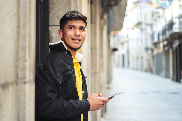 Man op straat van een stad met telefoon in de hand kijkend naar camera Latino man op straat met tablet in handen recht vooruit kijkend