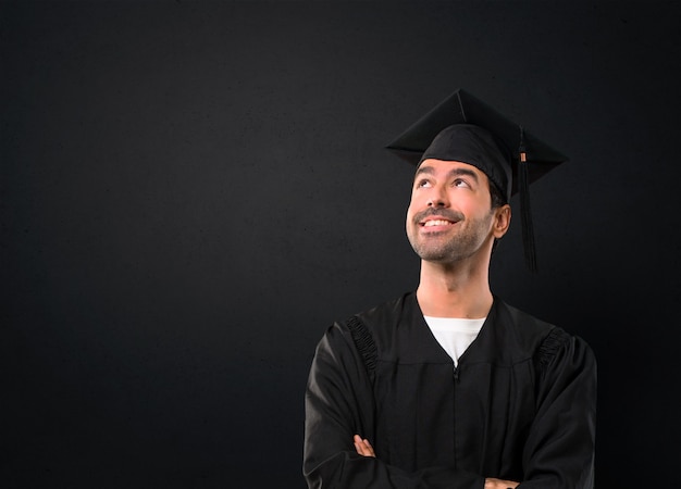 Man op zijn afstuderen dag Universiteit staan ​​en opzoeken terwijl lachend op zwarte achtergrond