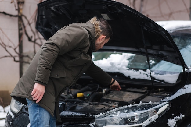 男は車のボンネットを開けて、車で何が起こっているのかを調べようとしています。冬の屋外