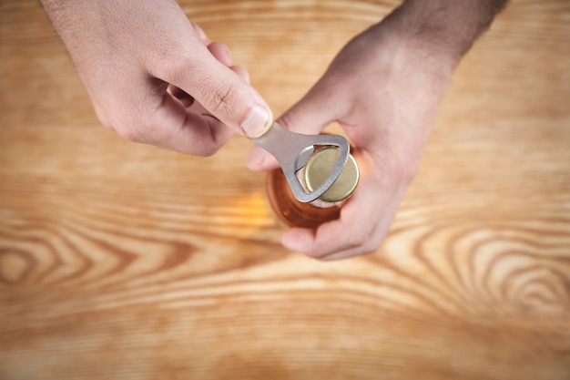 Man opening a bottle of beer on the wooden table.