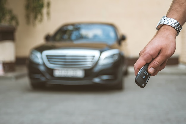 The man opens the car with a keychain, in the background is a black car.