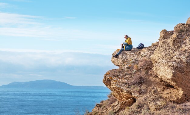 a man opens a thermos while sitting on the edge of a mountain