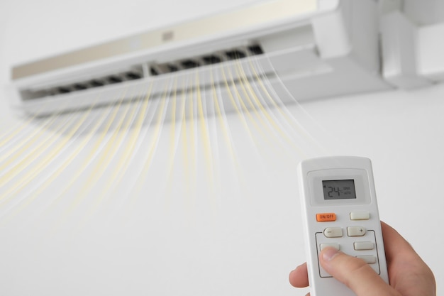 Man operating air conditioner with remote control indoors closeup