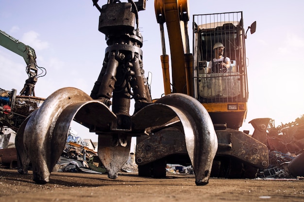 Macchina industriale dell'escavatore operativo dell'uomo utilizzata per il sollevamento di rottami metallici nel deposito di rifiuti