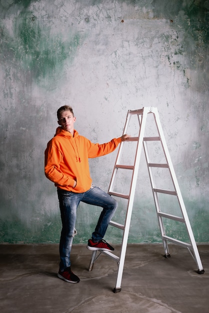 Man in an orange hoodie posing on a ladder