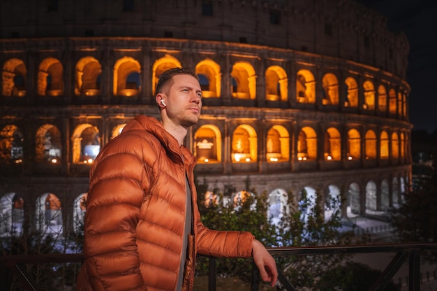 Man in orange jacket contemplating colosseum at night rome